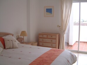A bedroom with a bed, a nightstand, a dresser, and a window with curtains.