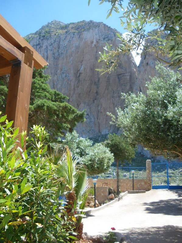 A courtyard with a wooden pergola, a stone wall, and a view of a mountain.
