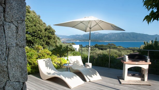 Una terraza con dos sillones, una mesa y una parrilla, con vistas panorámicas del mar y las montañas.