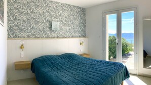 Un dormitorio con cama, una lámpara de pared, un radiador y vistas a través de un ventanal corredero.