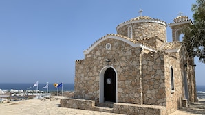 Eine Steinkirche mit einem Glockenturm und einer kleinen Kuppel in Strandnähe, mit Flaggen.