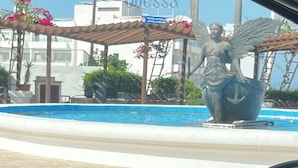 Ein Poolbereich mit einer Engelsstatue, umgeben von einer Pergola mit Blumen.