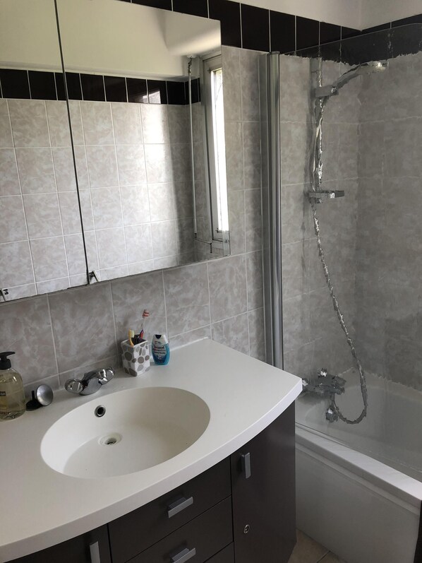 Un baño con lavamanos blanco, muebles oscuros, un espejo y una zona de ducha.