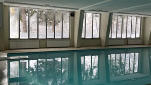 Uima-allas, jossa on suuret ikkunat, valkoiset seinät ja katto, jossa on näkyvissä olevat palkit.