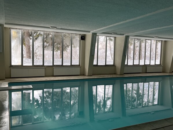 A swimming pool with large windows, white walls, and a ceiling with visible beams.
