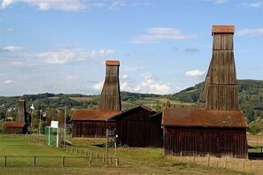 Ländliche Landschaft mit zwei großen Scheunen und einem kleineren Gebäude, umgeben von offenen Feldern und Hügeln.