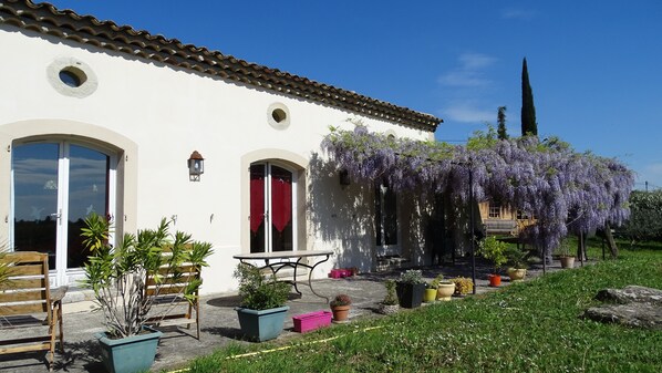A white building with a tiled roof, a red door, and a covered patio area with potted plants and a table.