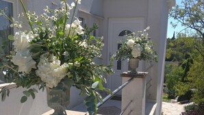 A building with a white facade, a tiled roof, and a staircase leading to a door. There are potted plants with white flowers on the steps. - Villa Sun - charming villa, heated pool, full privacy, wedding, near Dubrovnik (Cavtat)
