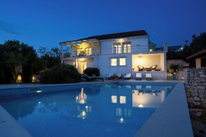 A two-story house with a swimming pool, outdoor seating, and a stone wall.