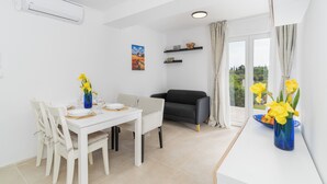 A dining area with a white table and chairs, a blue vase with flowers, a black sofa, and a window with curtains. - Villa Sun - charming villa, heated pool, full privacy, wedding, near Dubrovnik (Cavtat)