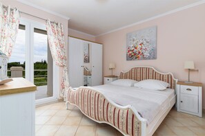 Un dormitorio con cama, mesita de noche, cómoda, ventana con cortinas y un cuadro en la pared.