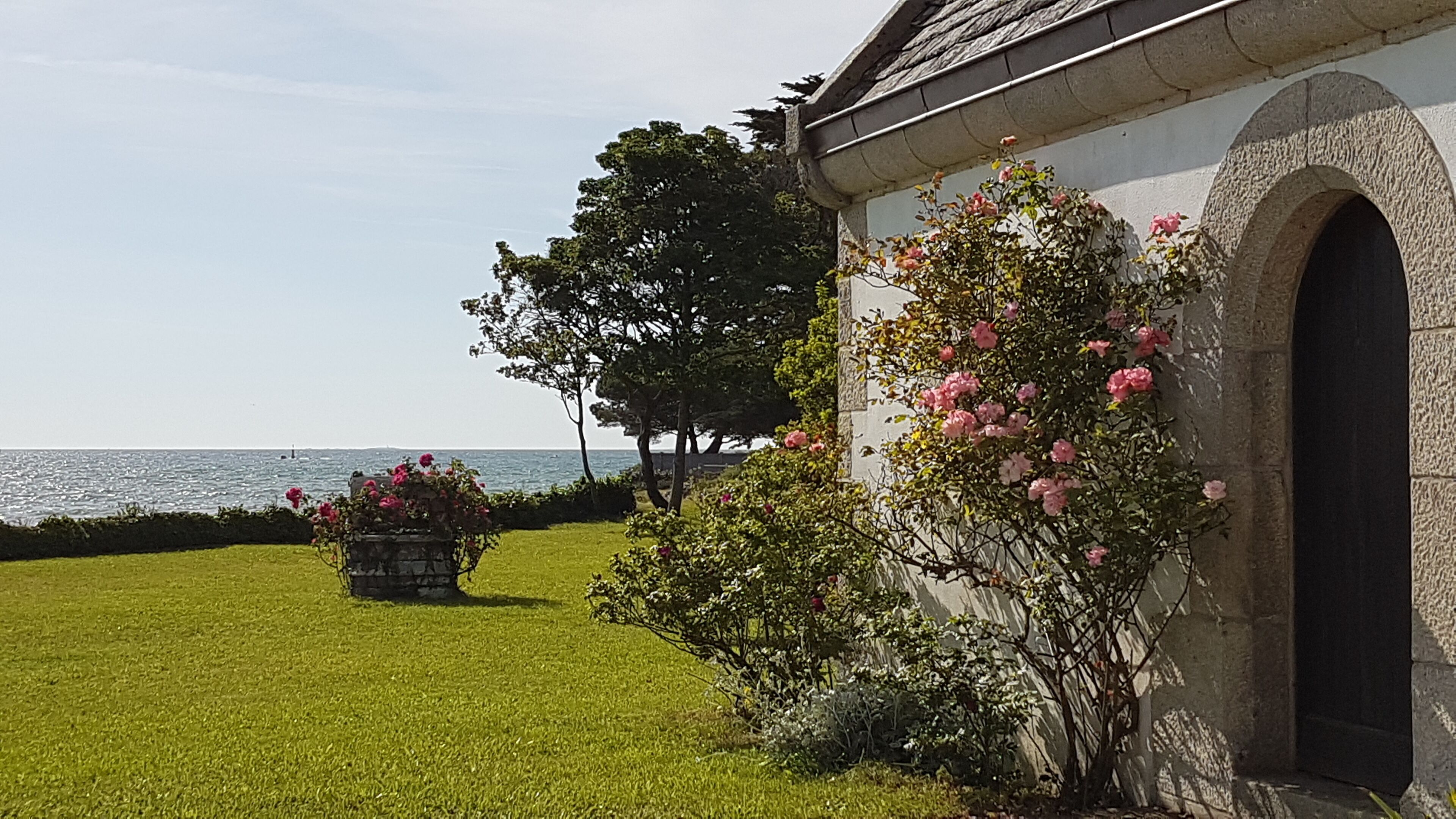 Ein Gebäude mit einer Stein-Fassade, einem Rasen und Blick auf das Meer.