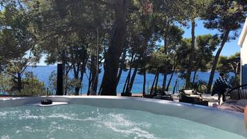 Relax in a serene outdoor setting with a hot tub surrounded by lush trees and a clear view of the sea.