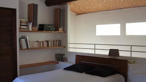 A bedroom with a bed, wooden headboard, built-in shelves with books and a radio, and a window with blinds. - Villa in the Luberon (Apt)