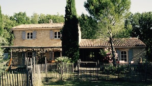 A stone house with a tiled roof, surrounded by a wooden fence and trees. - Villa in the Luberon (Apt)