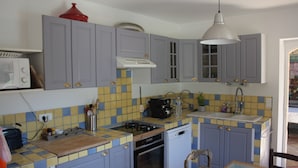 A compact kitchen with grey cabinets, a tiled backsplash, a gas stove, a dishwasher, and a coffee maker. - Villa in the Luberon (Apt)