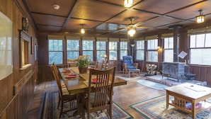 Interior acogedor de una cabaña con comedor, asientos, chimenea y ventanas amplias.