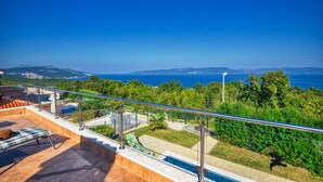 A rooftop terrace with a pool, outdoor seating, and a view of the sea and hills.
