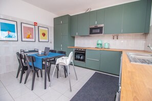 A compact kitchen with green cabinets, a microwave, a stove, and a coffee maker. There is a dining table with chairs and a laptop on it.