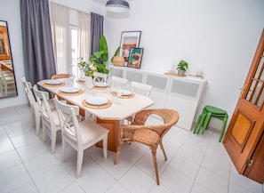 A dining area with a white table set for six, surrounded by white chairs and wicker chairs.