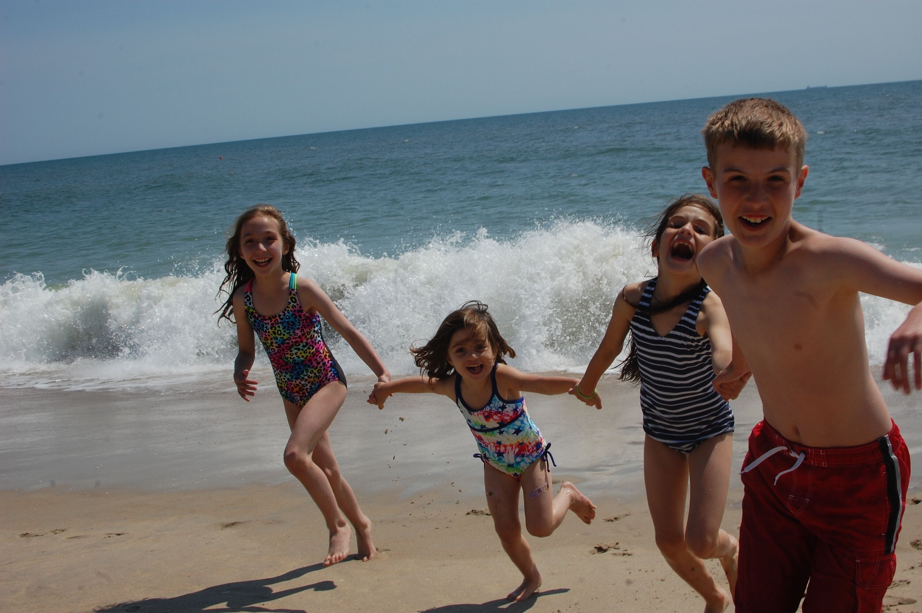 A beach scene with four people running towards the water.