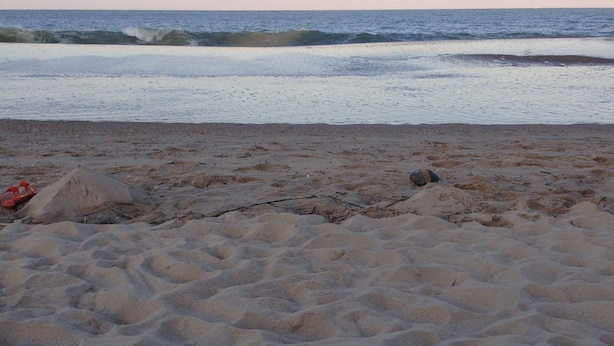 Ein sandiger Strand mit Fußspuren, die zum Wasser führen.