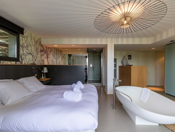 Une chambre moderne avec un grand lit, une baignoire blanche et un luminaire au plafond original.