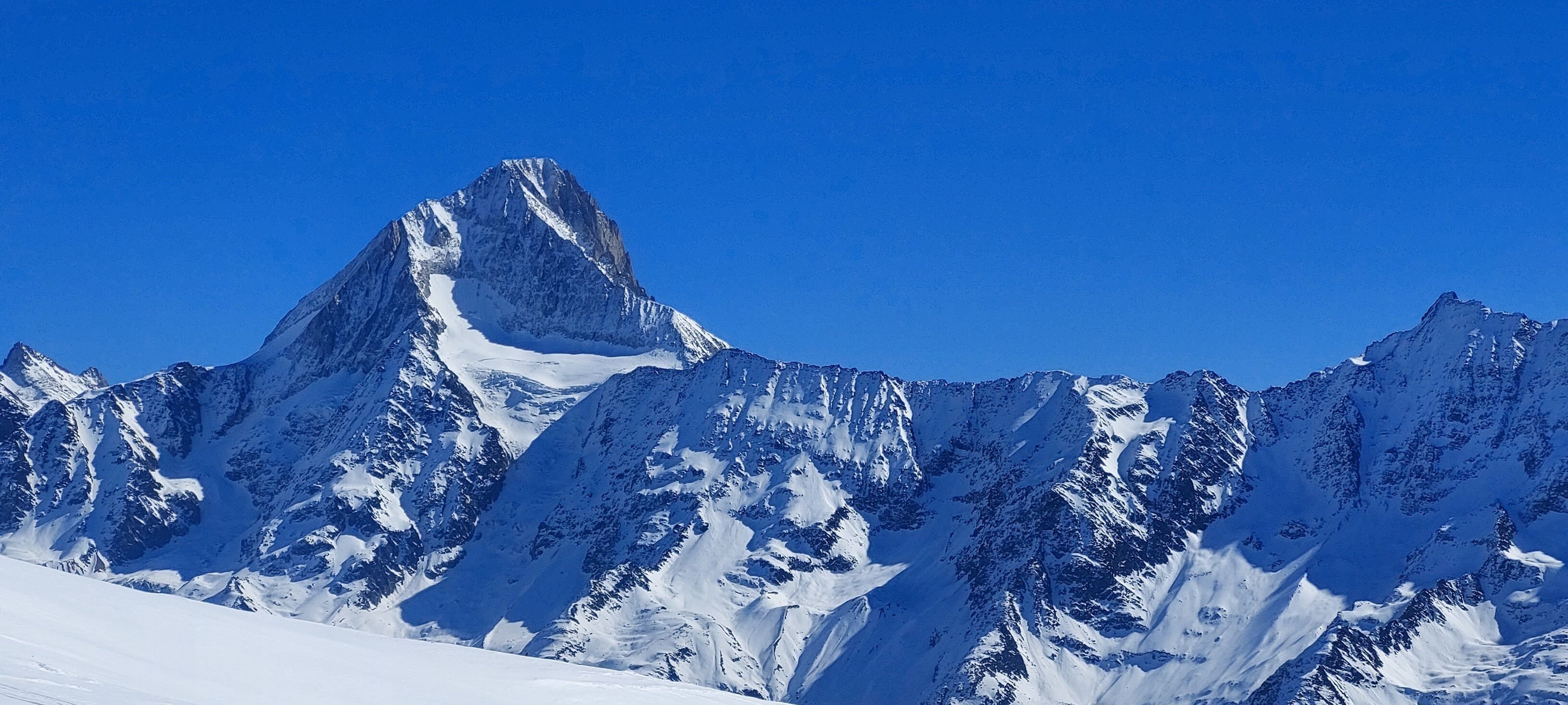 Ett snötäckt bergsmassiv med spetsiga toppar och en klarblå himmel.