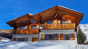 A wooden chalet with multiple balconies, large windows, and a snow-covered landscape.