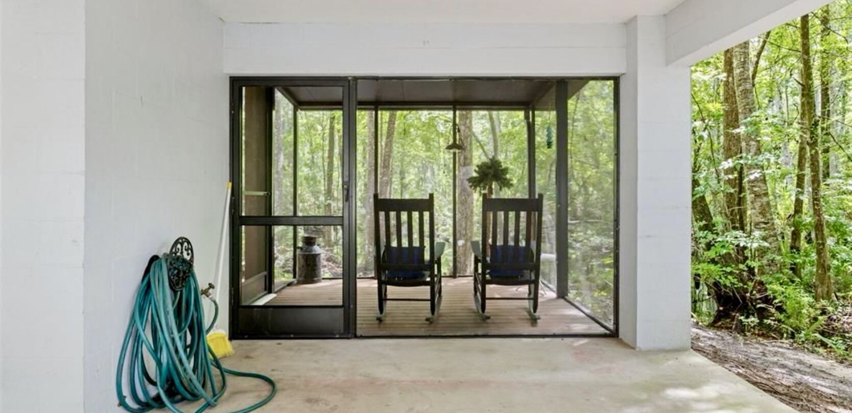 A covered outdoor seating area with two chairs and a hose on the left.