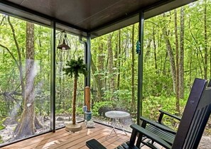 A wooden deck with a table and chairs, surrounded by glass walls offering a forest view. - WeekiWachee Retreat  “Relaxing cottage to get away from it all” (Weeki Wachee)