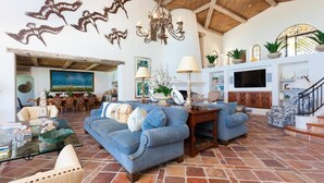 A spacious living room with a high ceiling, a fireplace, and a TV. There are sofas, a coffee table, and decorative items. - Beachfront Paradise! Please see instructions below prior to booking! (San Jose del Cabo)