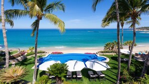 A swimming pool with lounge chairs and umbrellas, surrounded by palm trees and a view of the ocean. - Beachfront Paradise! Please see instructions below prior to booking! (San Jose del Cabo)
