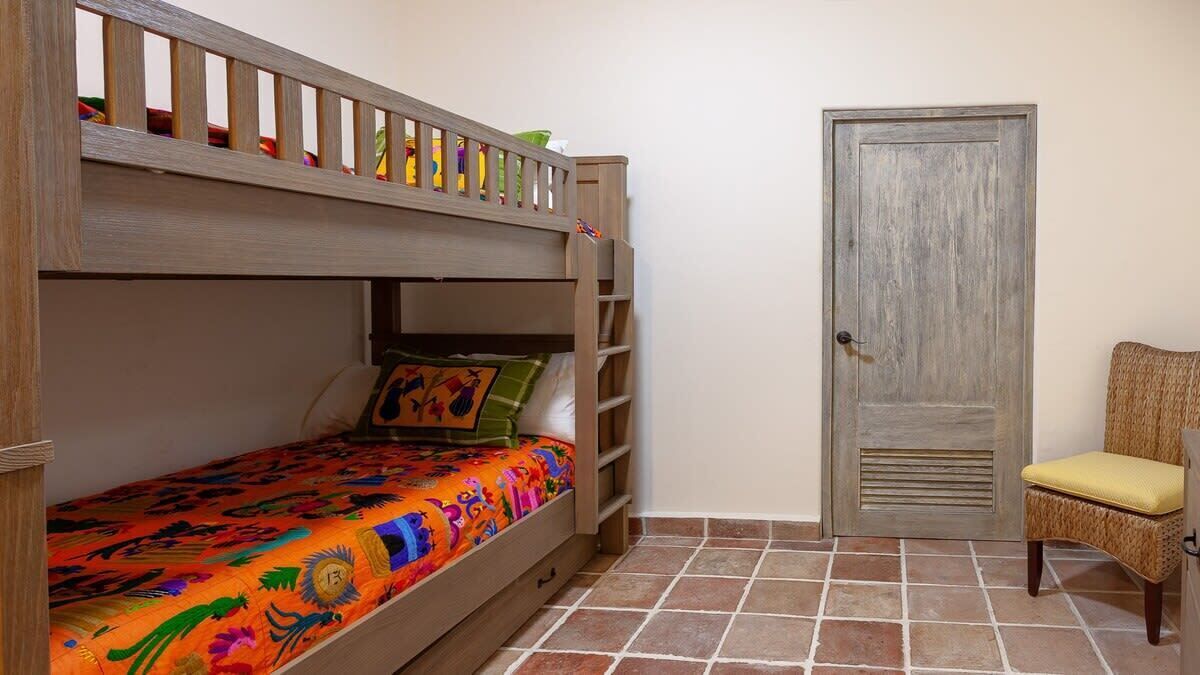 A bunk bed with a colorful bedspread, a wooden ladder, and a door with a textured panel.