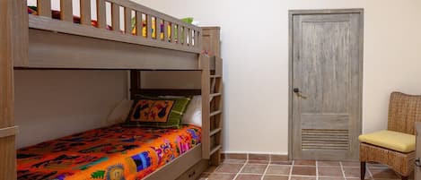 A bunk bed with a colorful bedspread, a wooden ladder, and a door with a textured panel.