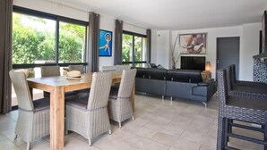 A modern living room with a wooden dining table, wicker chairs, a grey sofa, and a TV. - 4* architect's villa, contemporary, air-conditioned with heated swimming pool (Zonza)