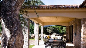 An outdoor patio with a stone wall, a wooden pergola, a dining table, and a sofa with cushions. - 4* architect's villa, contemporary, air-conditioned with heated swimming pool (Zonza)