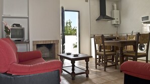 A living room with a fireplace, a dining area with a table and chairs, and a kitchen area with a microwave and stove. - Large community pool, beautiful outdoor kitchen with grill, private garden with garden furniture - Casa Marin 1 - (Conil de la Frontera)