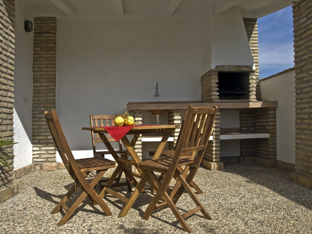 Een terras buiten met een bakoven, een houten tafel en stoelen.