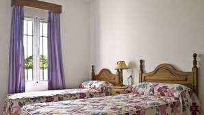 A bedroom with two single beds, a wooden headboard, a nightstand with a lamp, and a window with purple curtains. - Large community pool, beautiful outdoor kitchen with grill, private garden with garden furniture - Casa Marin 1 - (Conil de la Frontera)