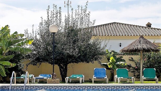 A pool area with lounge chairs, a thatched umbrella, and a building with a tiled roof. - Large community pool, beautiful outdoor kitchen with grill, private garden with garden furniture - Casa Marin 1 - (Conil de la Frontera)