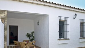 A white building with a covered patio area featuring wicker furniture and potted plants. - Large community pool, beautiful outdoor kitchen with grill, private garden with garden furniture - Casa Marin 1 - (Conil de la Frontera)