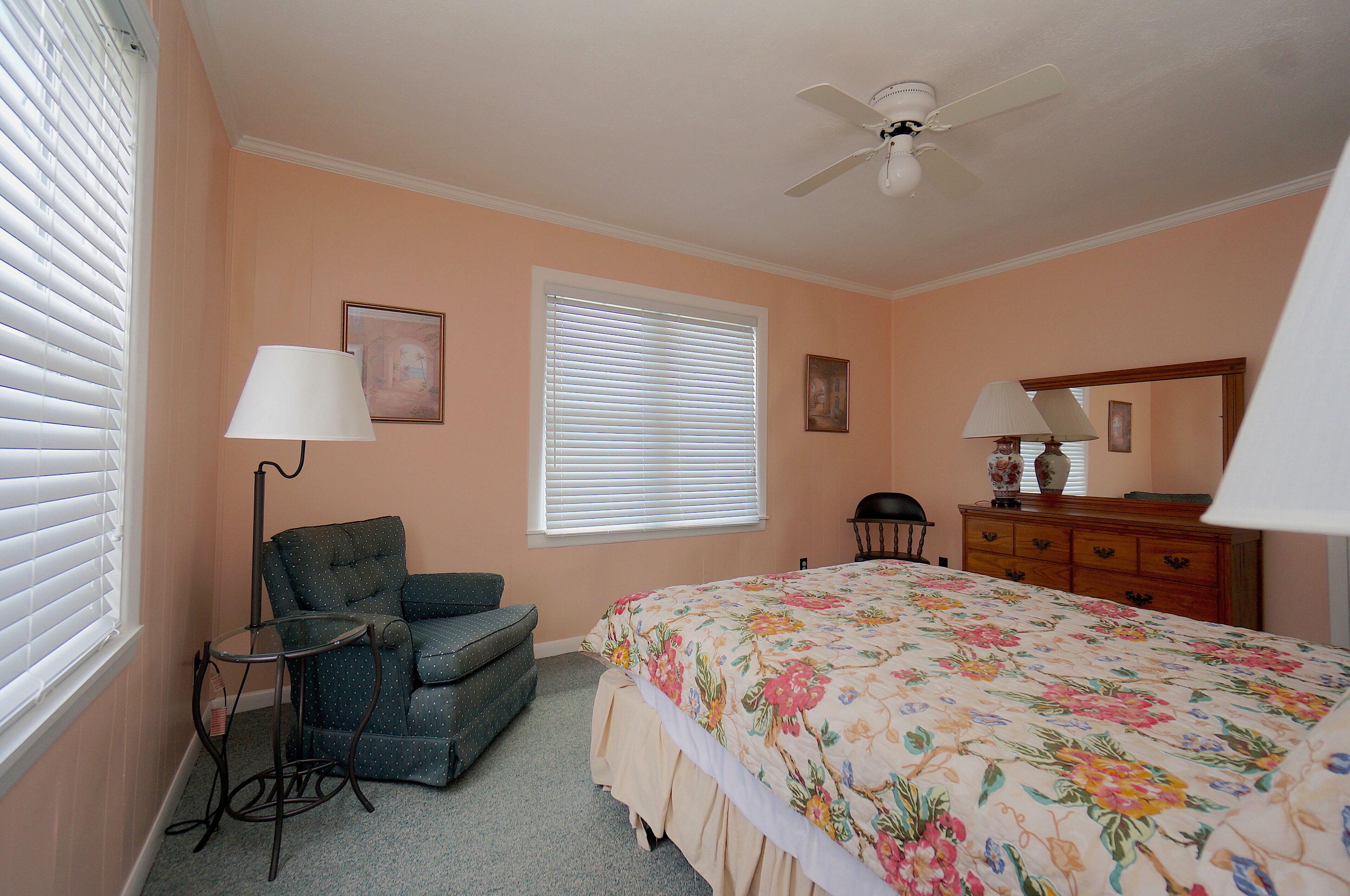 A bedroom with a bed, a chair, a dresser, a ceiling fan, and a window with blinds.