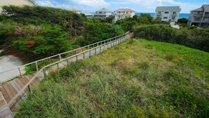 Una zona residenziale sul lungomare con una passerella in legno che conduce a una spiaggia, circondata da vegetazione rigogliosa e case con balconi vista mare.