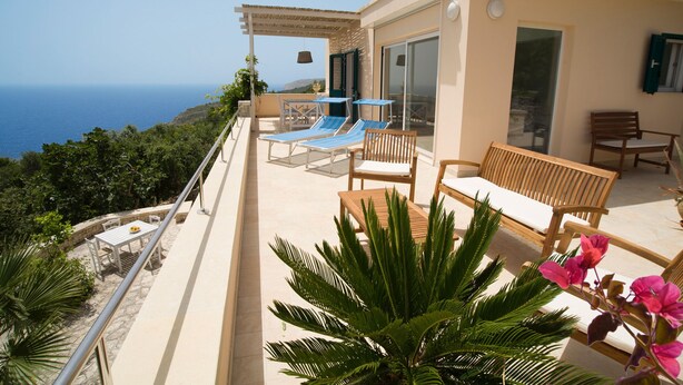 Un balcon avec vue sur la mer, une table avec des chaises et un banc en bois.