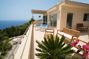 A balcony with a view of the sea, a table with chairs, and a wooden bench. - Beautiful villa with swimming pool and large terraces, for 6 to 8 people (Marina di Novaglie)