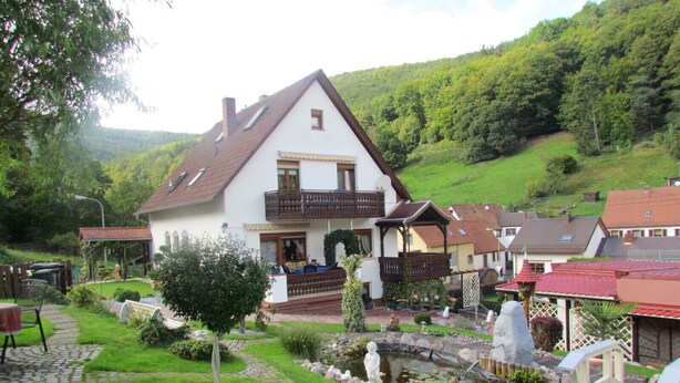 A two-story house with a balcony, surrounded by a garden with a pond, a statue, and a small bridge. - well-equipped apartment in a quiet forest location (Ramberg)