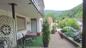 A covered patio area with a table and chairs, surrounded by potted plants and a small garden. - well-equipped apartment in a quiet forest location (Ramberg)