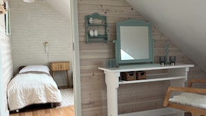 Un dormitorio con techo inclinado, una cama, un escritorio con espejo y una silla.