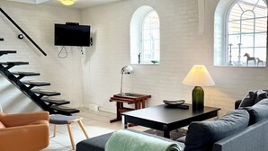 Una sala de estar moderna con una escalera, un televisor de pantalla plana, una lámpara y un sofá con una manta.